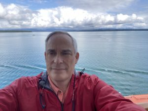 a photo selfie of robert wearing a red jacket with a calm body of water in the background